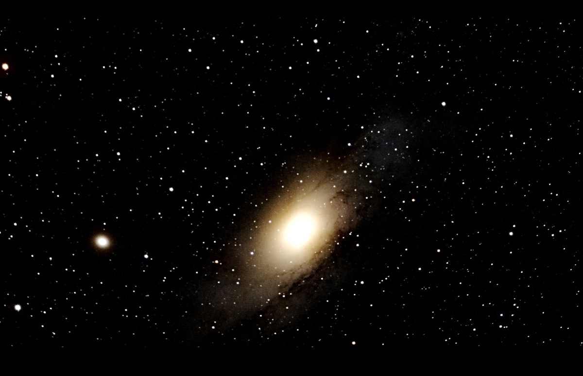 The Andromeda Galaxy, a bright spiral core with a dust lane and two companion galaxies.